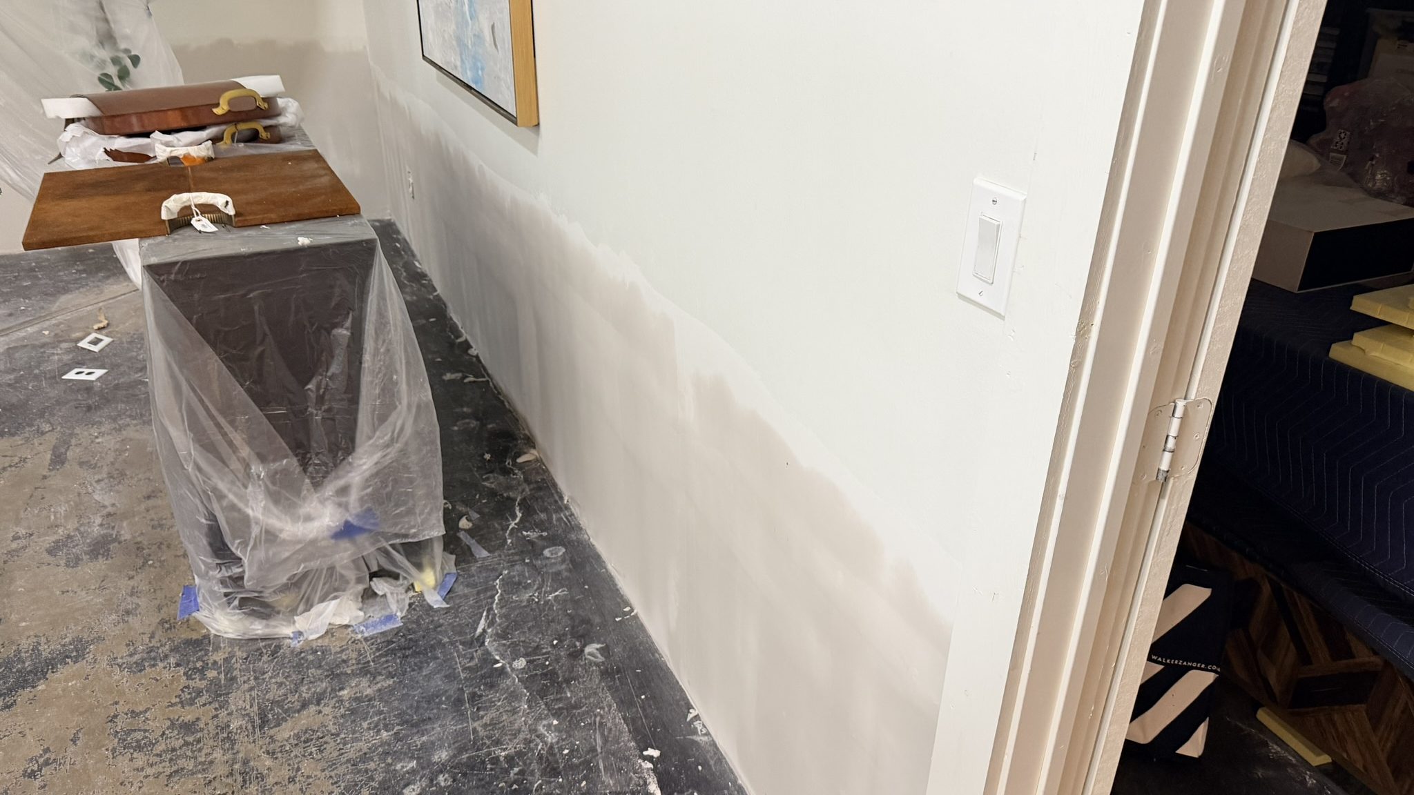 Flood-cut repair band along the base of a wall with furniture wrapped in plastic after a water loss in a DFW building