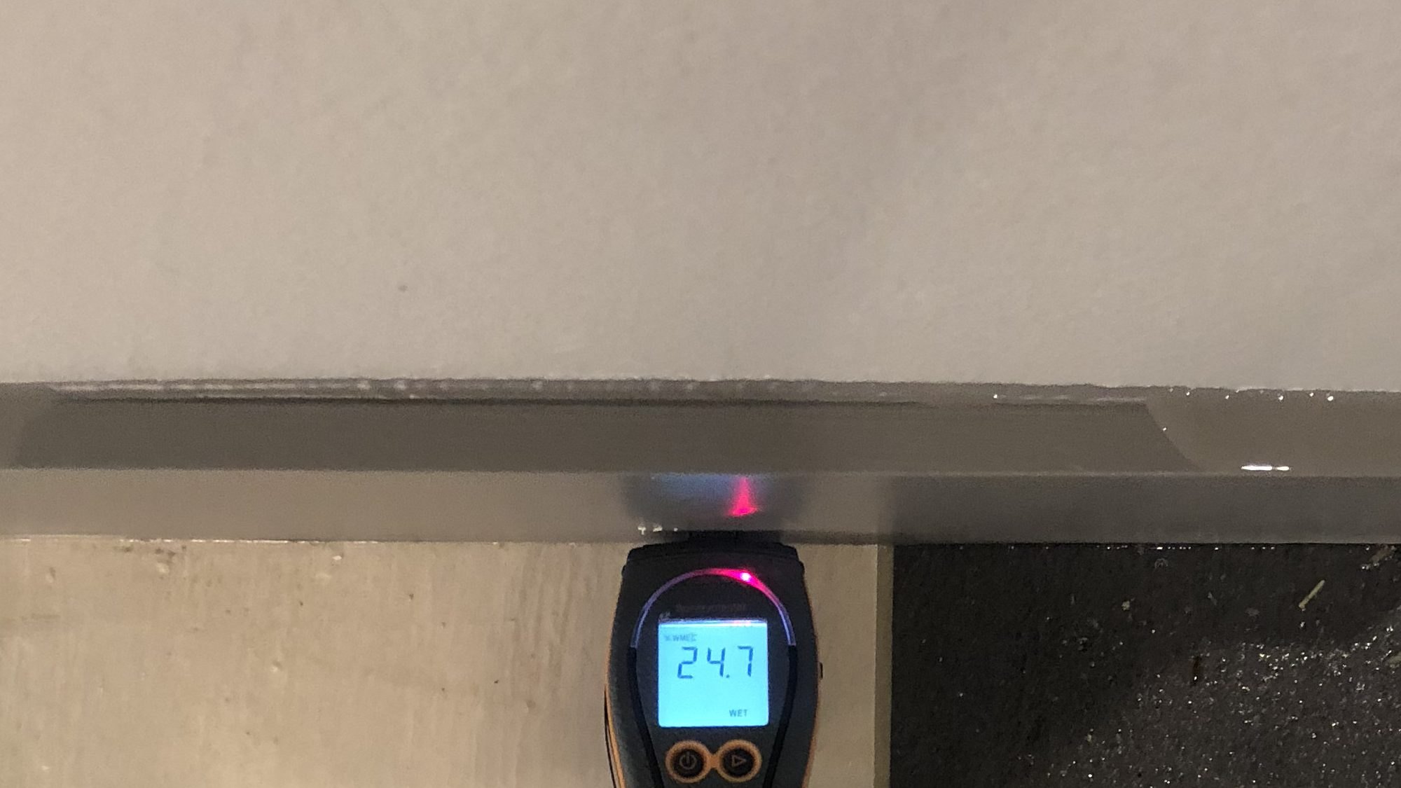 Moisture meter reading WET at the base of a finished wall above a wet floor after heavy rain in a DFW home